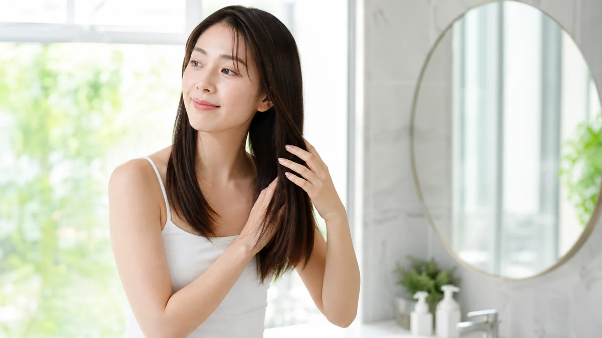 朝の洗面所でストレートヘアを手ぐしで整えている女性