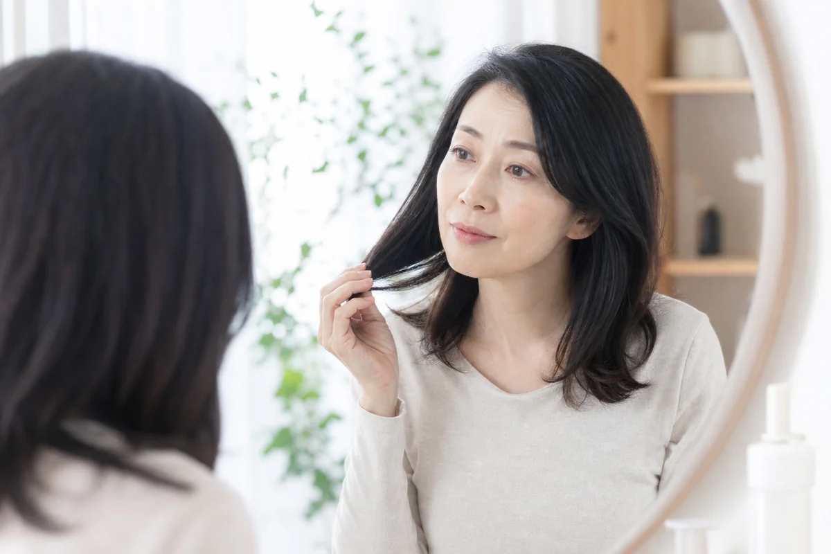 鏡の前で黒髪を手にとって見つめる女性