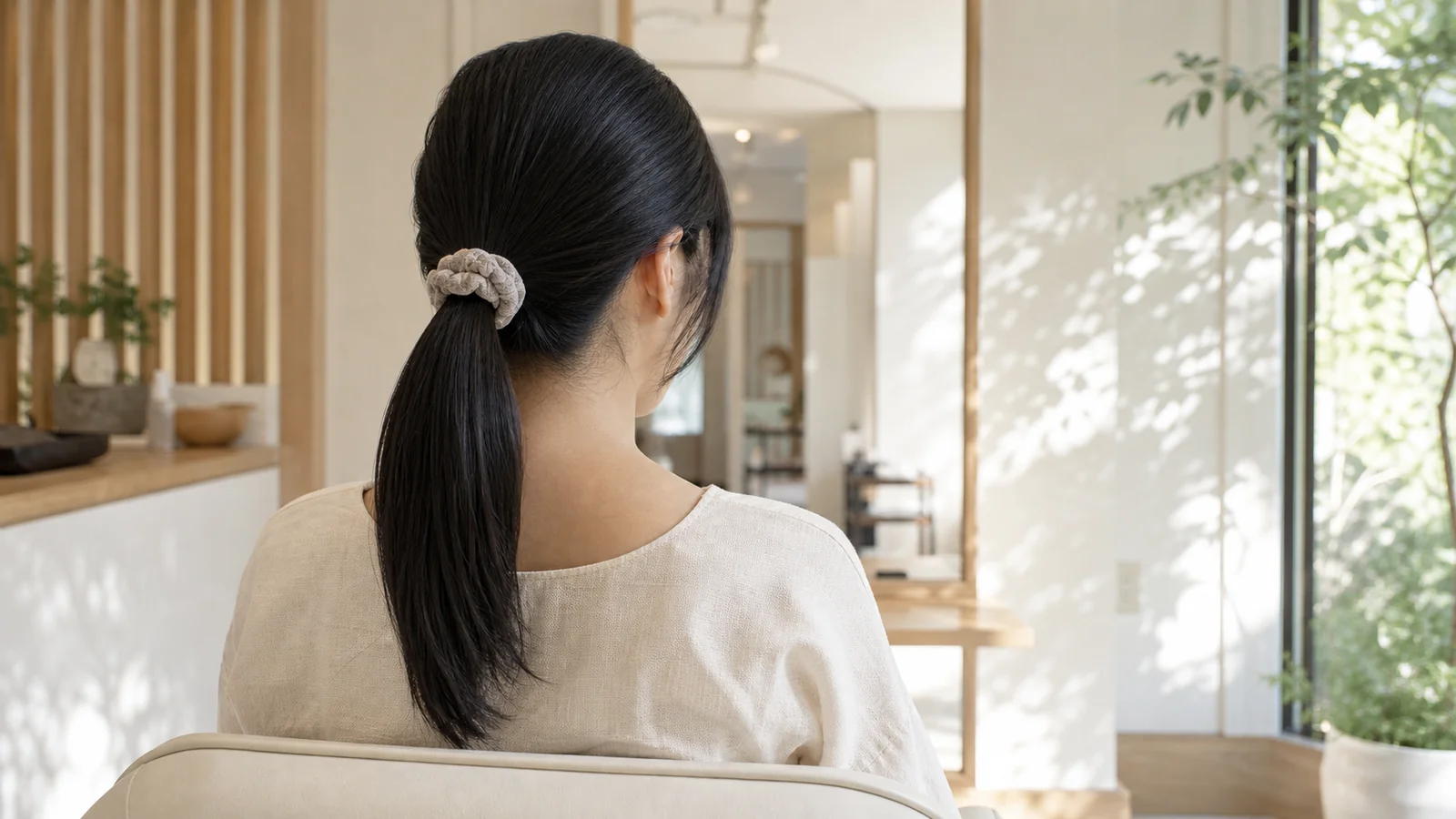 夏の朝、ストレートヘアをゆるくひとつに結ぼうとしている女性